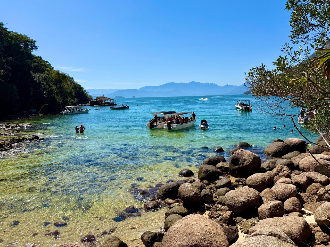 Vista da praia, das águas cristalinas, das pedras e das embarcações